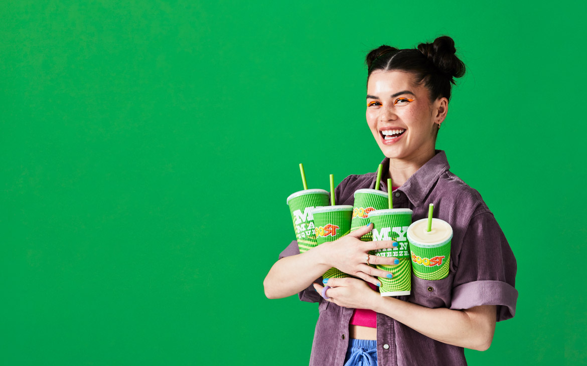 Smiling woman holding an armful of Boost Juice smoothies against a bright green backdrop